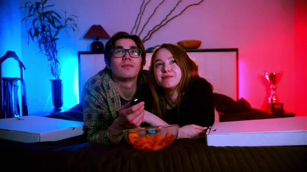 웃고 있는 젊은 부부가 침대에 누워 영화를 보고 있습니다 — 스톡 사진