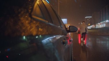 Açık renk ceketli yakışıklı bir genç arabaya koşuyor ve oturuyor.