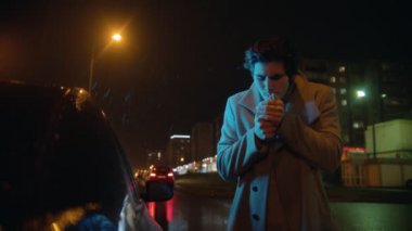 Genç ve şık bir adam gece dışarıda sigara yakıyor.