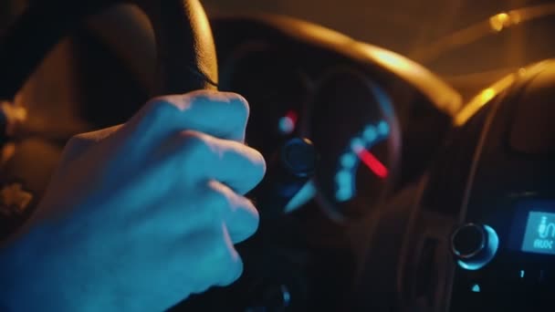 Jonge man die 's nachts een auto bestuurt - stuur in geel en blauw licht — Stockvideo