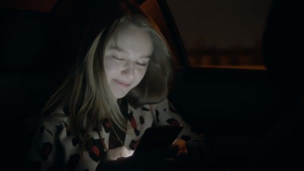 Mladá usměvavá žena na zadním sedadle auta a píše někomu — Stock video