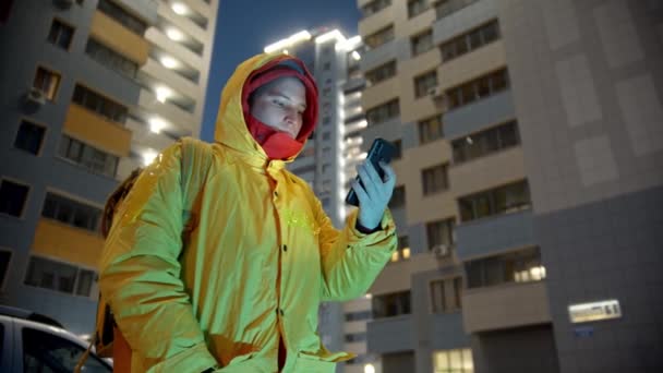 Liefermann in gelber Kleidung hält sein Handy in der Hand und versucht, den Standort zu finden — Stockvideo