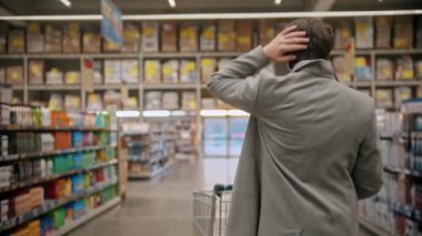 Koruyucu maskeli genç adam büyük marketin farklı bölümleri arasında yürüyor.