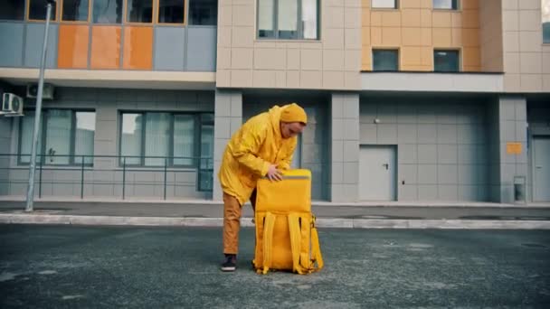 Man kurir i gula kläder levererar mat - öppnar upp sin ryggsäck drar ut pizza lådor och släpper dem på golvet — Stockvideo