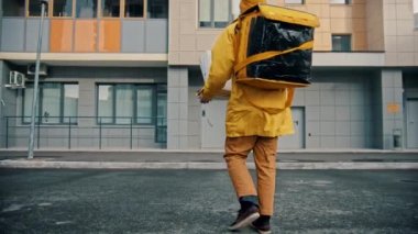 Sarı elbiseli bir kurye yiyecek getiriyor yere pizza kutularını bırakıyor ve teslimata devam ediyor.