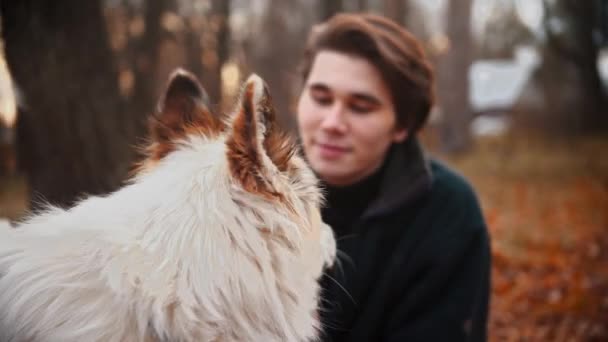 Joven con su hermano acariciando perro al aire libre en otoño — Vídeo de stock