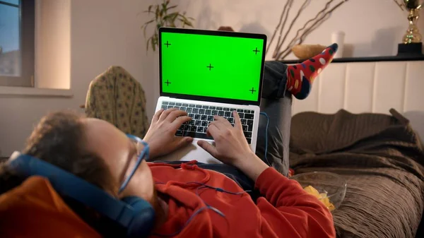 Hombre joven acostado en la cama con el ordenador portátil - pantalla verde —  Fotos de Stock