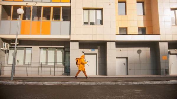 O mensageiro de homem em roupas amarelas oferece comida andando perto do alpendre — Fotografia de Stock