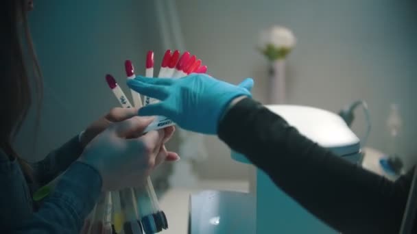 Manicura maestra y joven mujer eligiendo el color del esmalte de uñas en las muestras rojas — Vídeos de Stock