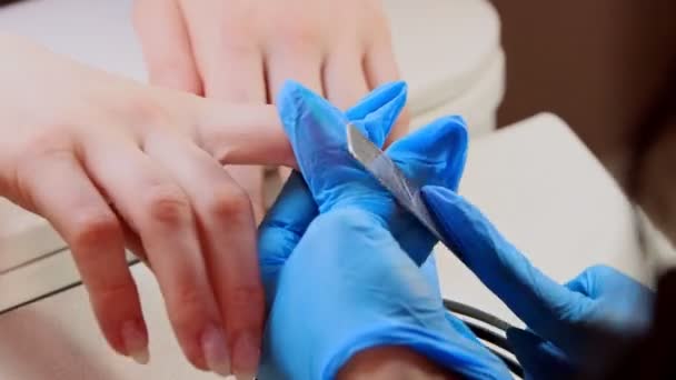 Manicure master in blue gloves doing manicure - filing the nails — Stock Video