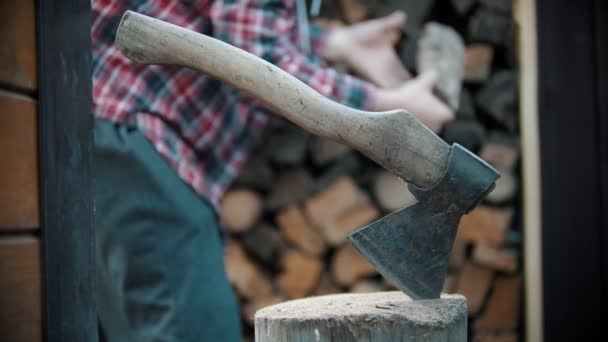 Young man woodcutter putting logs on the stand - the ax is stuck in the log stand — Stock Video