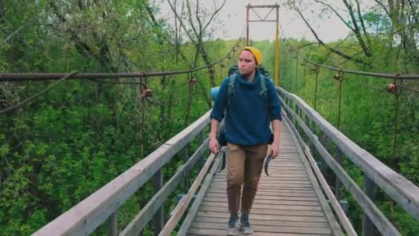 Ung man resenär med en stor ryggsäck promenader på bron i skogen — Stockvideo