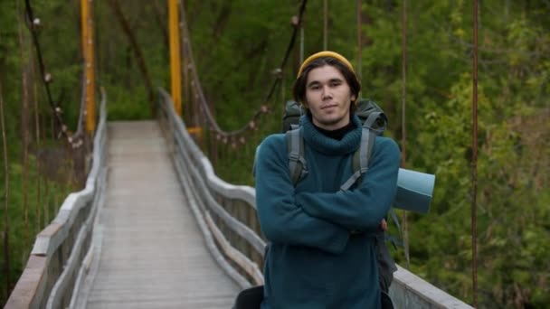 Młody mężczyzna podróżnik stojący na moście i patrzący w kamerę — Wideo stockowe