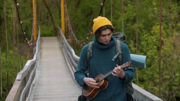 Joven viajero de pie en el puente y jugando ukelele — Vídeo de stock