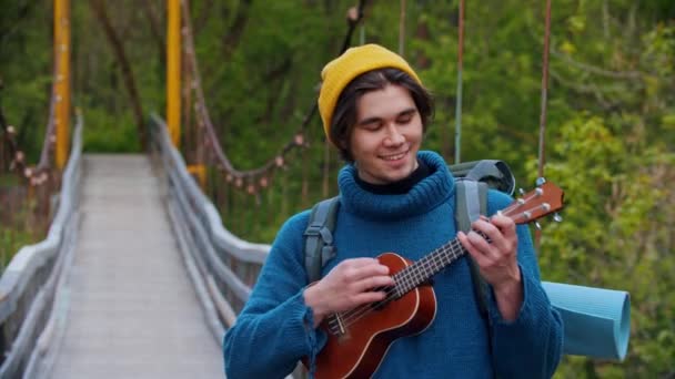 若いです笑顔男旅行者立ってオンザブリッジと演奏ウクレレ — ストック動画