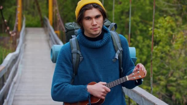 Joven viajero sonriente de pie en el puente y sosteniendo ukelele — Vídeo de stock