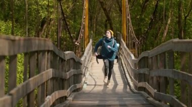 Ormandaki köprüde koşan büyük sırt çantalı genç bir gezgin.
