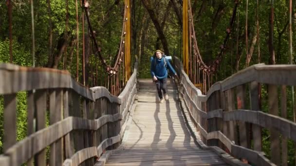 Hombre joven viajero con gran mochila corriendo en el puente en el bosque verde — Vídeo de stock