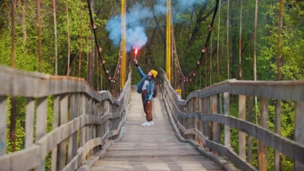 Giovane donna sorridente in piedi sul ponte nella foresta estiva con un fuoco sollevato — Video Stock