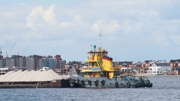 Транспортное судно, перевозящее камни через реку на фоне современных зданий — стоковое видео