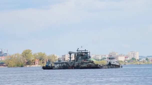 Транспортное судно, перевозящее камни через реку на фоне зданий — стоковое видео