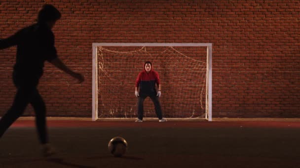 Dos jóvenes jugando al fútbol en el patio de recreo por la noche - un hombre tratando de proteger las puertas — Vídeo de stock