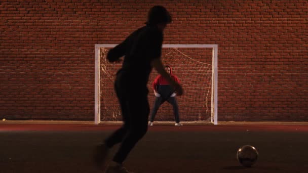 Dos jóvenes amigos jugando al fútbol en el patio de recreo por la noche - un hombre protegiendo las puertas — Vídeos de Stock