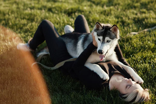 Beautiful young woman playing with funny husky dog with different eyes outdoors at park