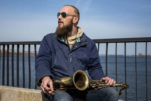 Şehrin sokaklarında gözlüklü yakışıklı bir erkek saksafoncu oynuyor.
