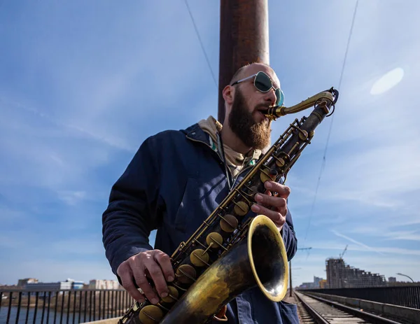 Şehrin sokaklarında gözlüklü yakışıklı bir erkek saksafoncu oynuyor.
