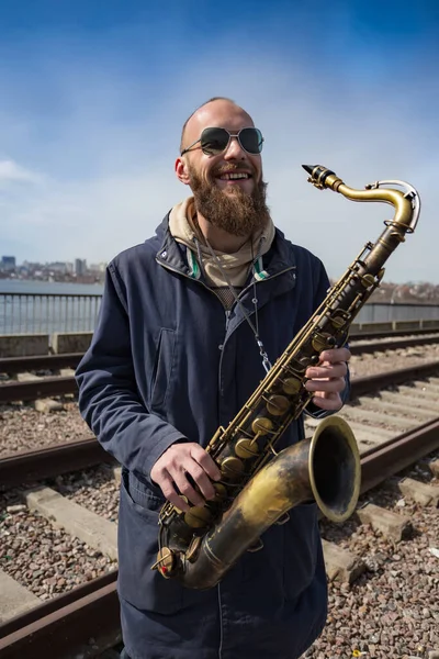 Şehrin sokaklarında gözlüklü yakışıklı bir erkek saksafoncu oynuyor.