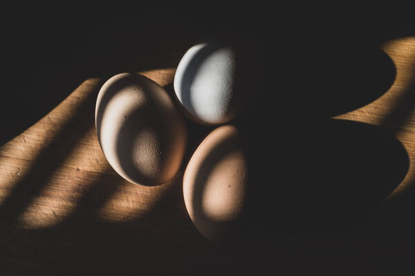 три свежих куриных яйца лежат на деревянной доске, тепло освещенной красивым теплым светом
