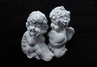 Siyah arka planda iki beyaz melek figürü birbirleriyle konuşuyor gibi görünüyor.. 