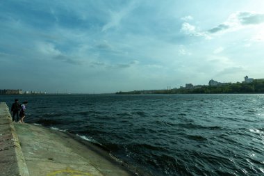 Körfezde beton iskele, dalgalar, uzaktan aşıklar. Genç adam kız arkadaşını destekliyor.. 