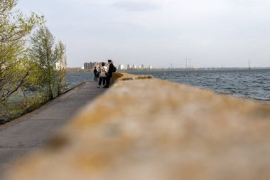 Körfezde beton iskele, dalgalar, uzaktan aşıklar. Genç adam kız arkadaşını destekliyor.. 