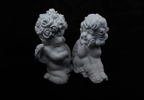 Karanlık arka planda iki beyaz melek figürü birbirleriyle konuşuyor gibi görünüyor. Alçıdan ya da seramiklerden yapılmış.