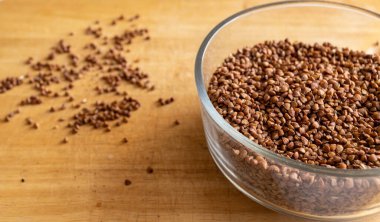 Şeffaf derin bir kasede çiğ karabuğday. Tohumlar dikkatsizce etrafa saçılmıştır. Mutfak masası. Gün ışığı