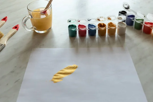 different colors of paint on a light table. a piece of paper for drawing. the brushstroke applied to it. the brushes are lying on the table and the water in the glass is colored with the brush lowered into it
