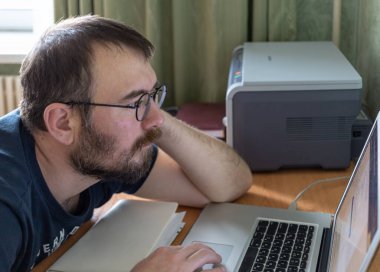 Sakallı çekici bir adam dikkatle dizüstü bilgisayarın ekranına bakıyor. ev ofisi