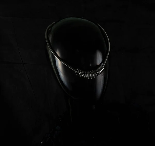 Sıra dışı bir şekilde elle yapılan bir kolye, bir manken kadının portresi olarak sunuluyor. Koyu bir arka planda ve arkada işaretli olan kolye parıldıyor. Yansımalar. Değerli taş ya da metal değil.