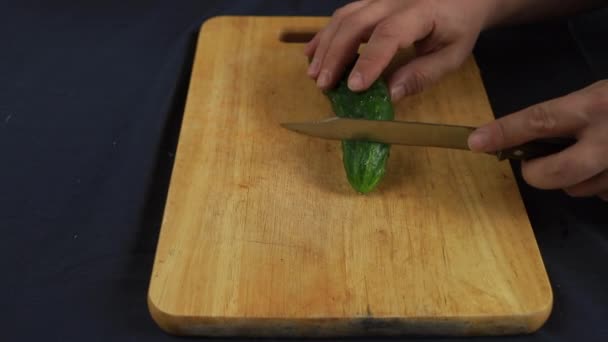 På en träskiva, skär en grön gurka i stora runda delar. Starka händer, vass kniv. Det finns en bordsduk på bordet. kvinna på ett kök — Stockvideo