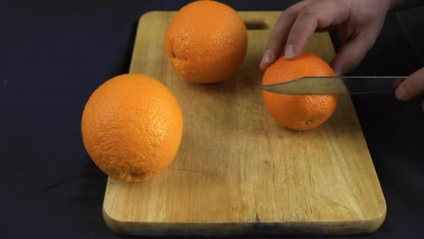 Una naranja jugosa se corta en rodajas redondas grandes en una tabla de madera. Manos fuertes, cuchillo afilado. Hay un mantel sobre la mesa. . — Vídeos de Stock