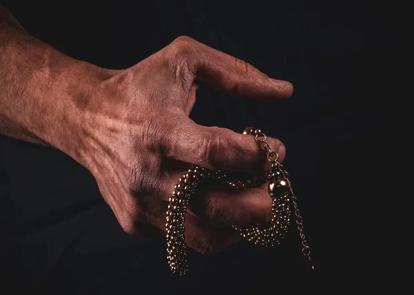 Güçlü erkek çalışan eller, karanlık bir arka planda parlak mücevherleri zıt tutarlar. Kollarda dövmeler var. Eller mücevherleri yırtıyor