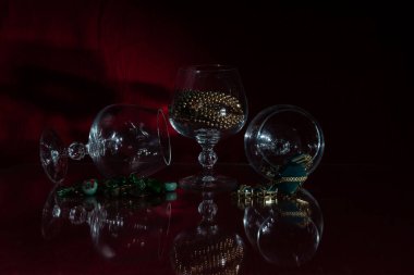 Üç boş bardak, kostüm mücevherleri, camda yansımalar, koyu kırmızı arka plan.