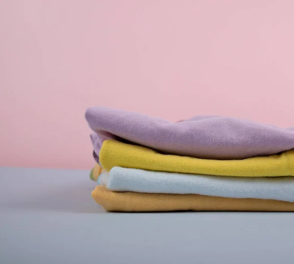 Çamaşır makinesinden sonra çocuk kıyafetleri. Demir giysiler bir yığın giysi içinde katlanır & yumuşak pembe arkaplan rengi