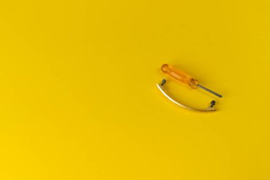 Turuncu saplı bir tornavida ve cıvatalı bir dolap kolu. Yanında vida ve tornavida olan bir dolap için. sarı arkaplan