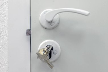 Kapı kolu, kilit, anahtar ve beyaz kapı.