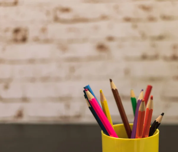 colored pencils in a cup on a black table against the background of a brick wall