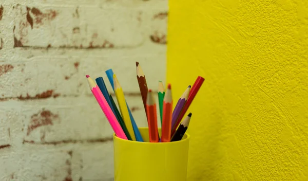 Цветные карандаши в чашке на черном столе на фоне кирпичной стены — стоковое фото