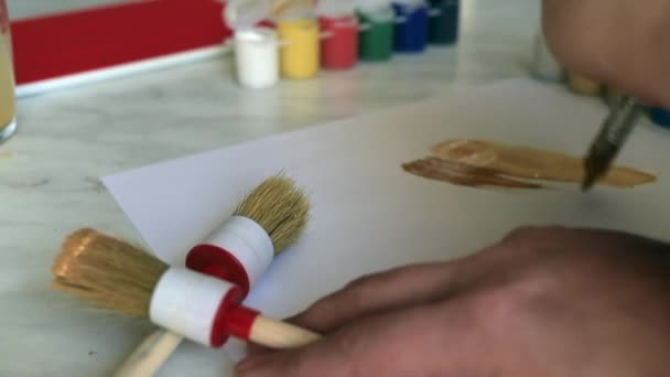 Handen verven met een penseel en verven op een stuk papier — Stockvideo